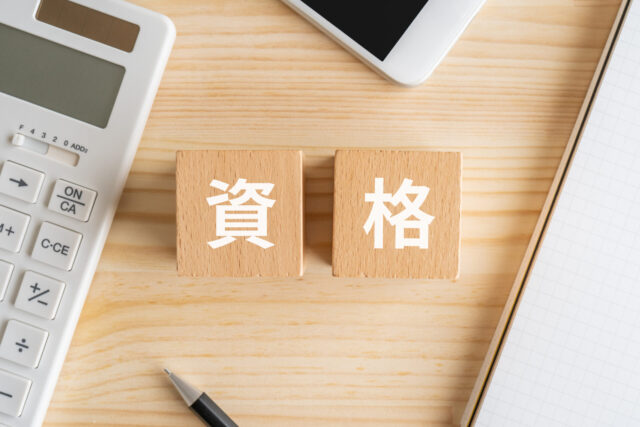 資格と書かれたブロック、電卓、スマホ、ノート